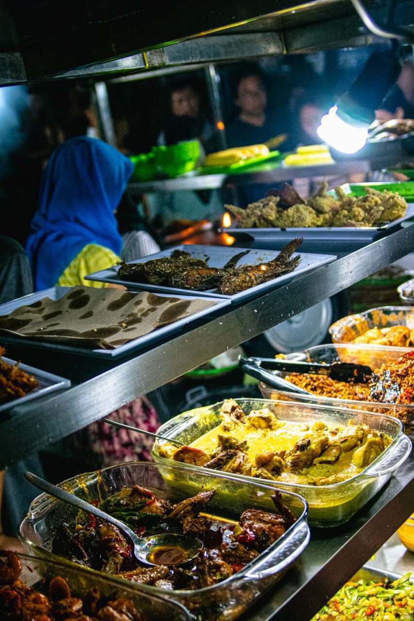 Stoisko na nocnym targu Gili Trawangan z tacami pełnymi indonezyjskich potraw, smażonych ryb i dań curry, przygotowywanych przez lokalnych sprzedawców.