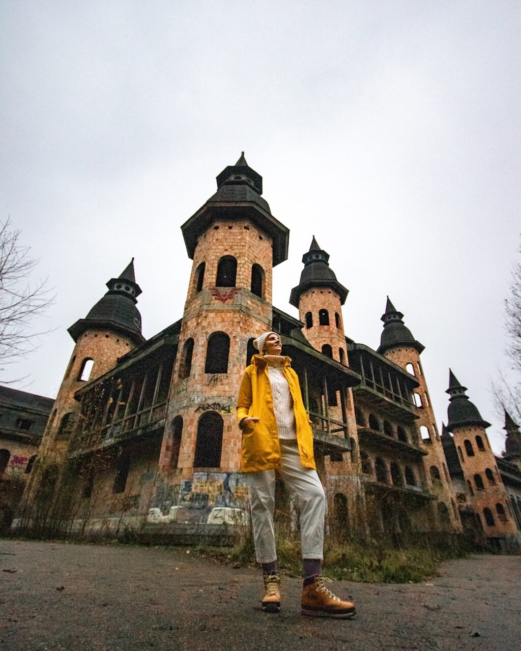 Kobieta w żółtej kurtce stoi przed nawiedzonym Zamkiem w Łapalicach w Polsce
