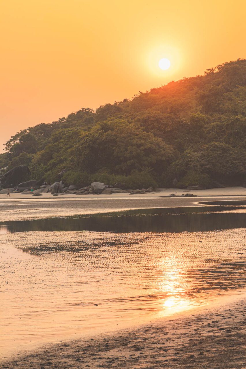 Sunset over the hills and bay of Palolem, Goa, reflected in the water