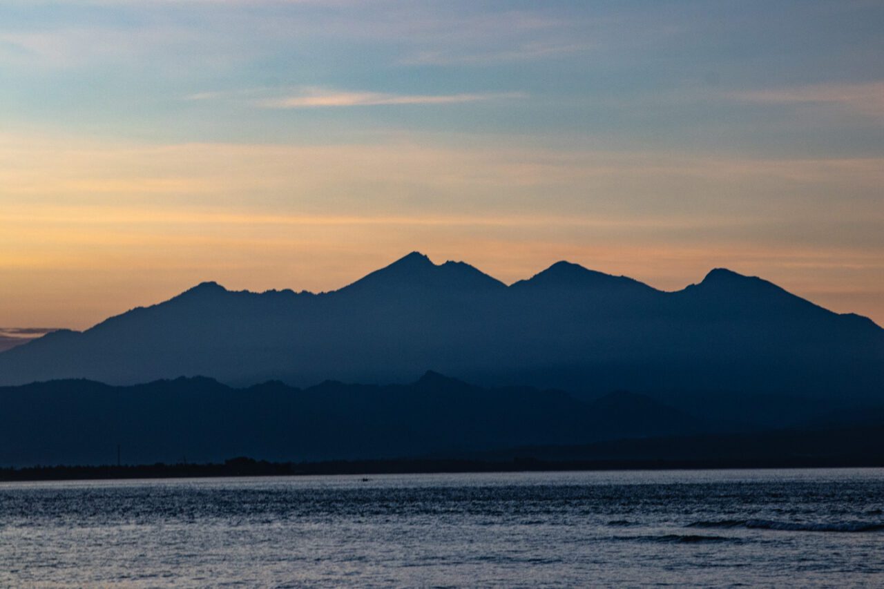 View of Lombok’s mountains at dawn, with soft sunrise light and a calm sea in the foreground.