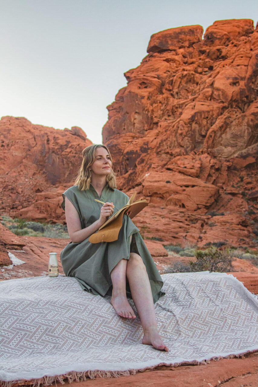Anna Flik journaling barefoot on a desert mat in Arizona, with a bottle of Butta - soulful morning ritual by travel blogger Runaway Ann.