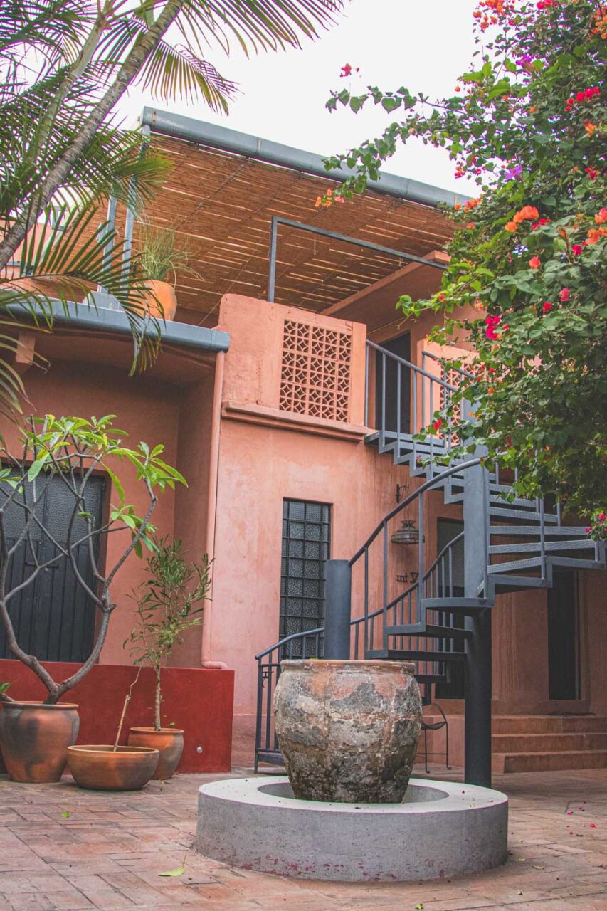 Dziedziniec hotelu w Oaxaca z okrągłą studnią, spiralnymi schodami i donicami z roślinami tropikalnymi