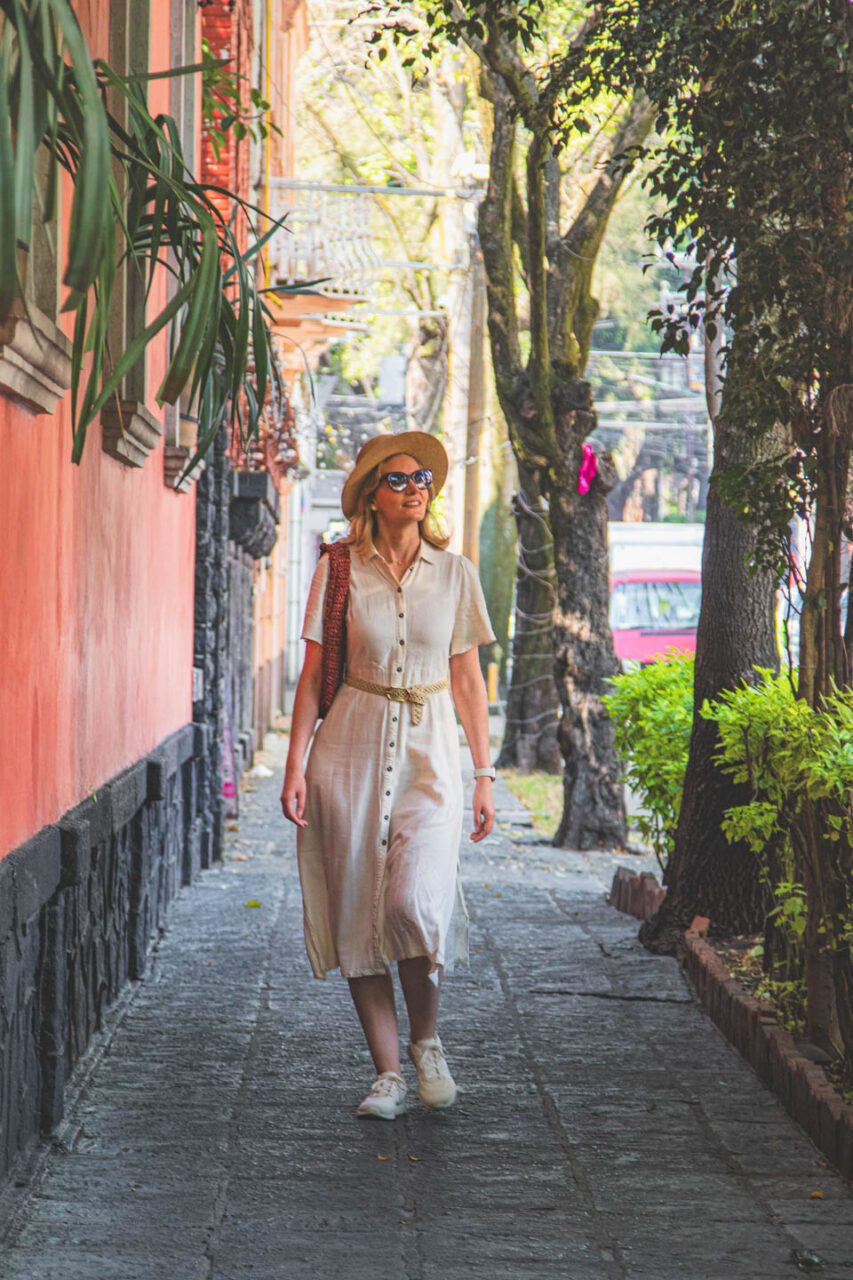 A walk through the Coyoacán district in Mexico City. A woman walks down a narrow street among colorful walls and greenery, in the peaceful atmosphere of the neighborhood.