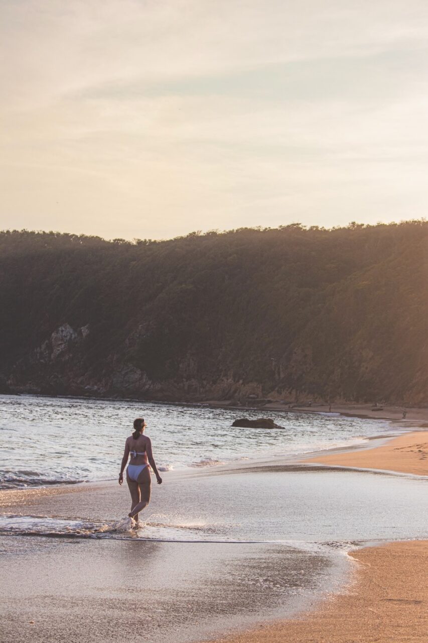 A woman walking alone along the shoreline on a quiet Mexican beach at sunset