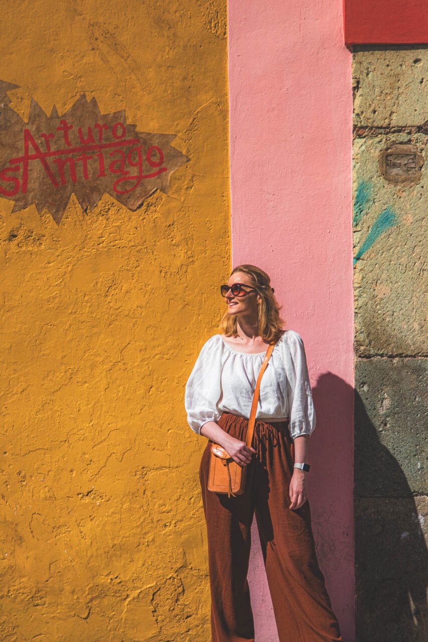 A woman stands in front of a colorful wall in Oaxaca de Juárez, Mexico, in the city's historic district.