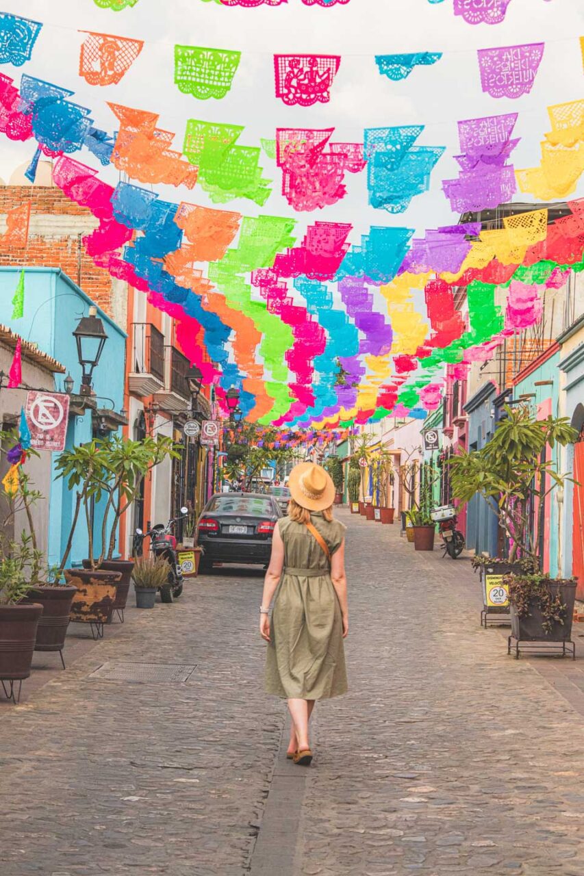 A walk along a colorful street in Oaxaca de Juárez, Mexico, with traditional papel picado hanging above the cobblestone street.