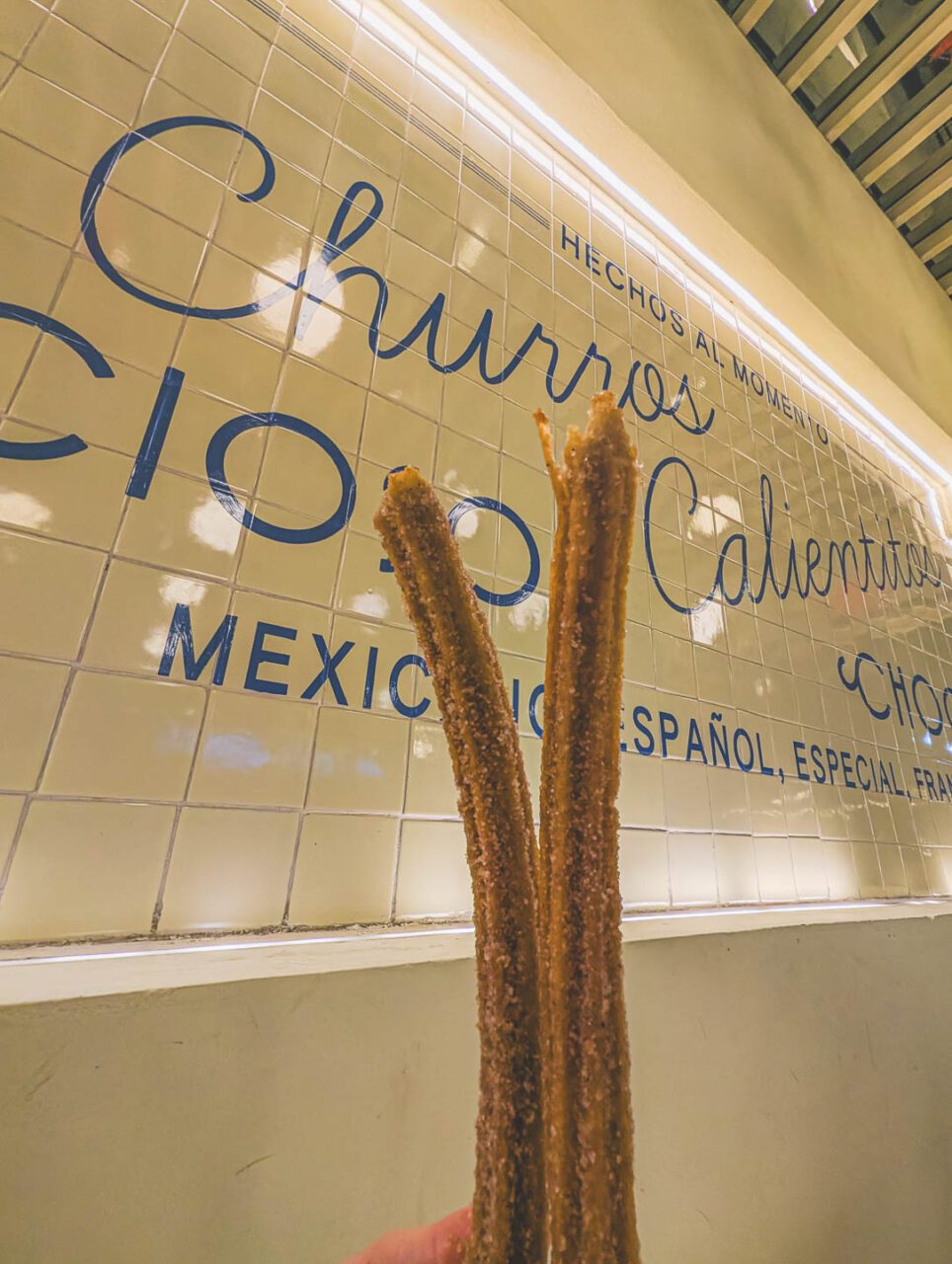 Churros from El Moro Churrería in Mexico City, held in hand against the background of the restaurant's tiled wall.