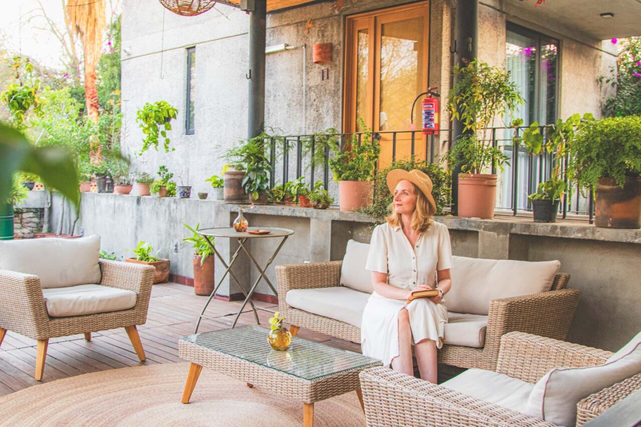 The terrace at Casa Tuna in the Coyoacán district of Mexico City. Rattan armchairs, a coffee table, plants, and a peaceful, green space for relaxation.