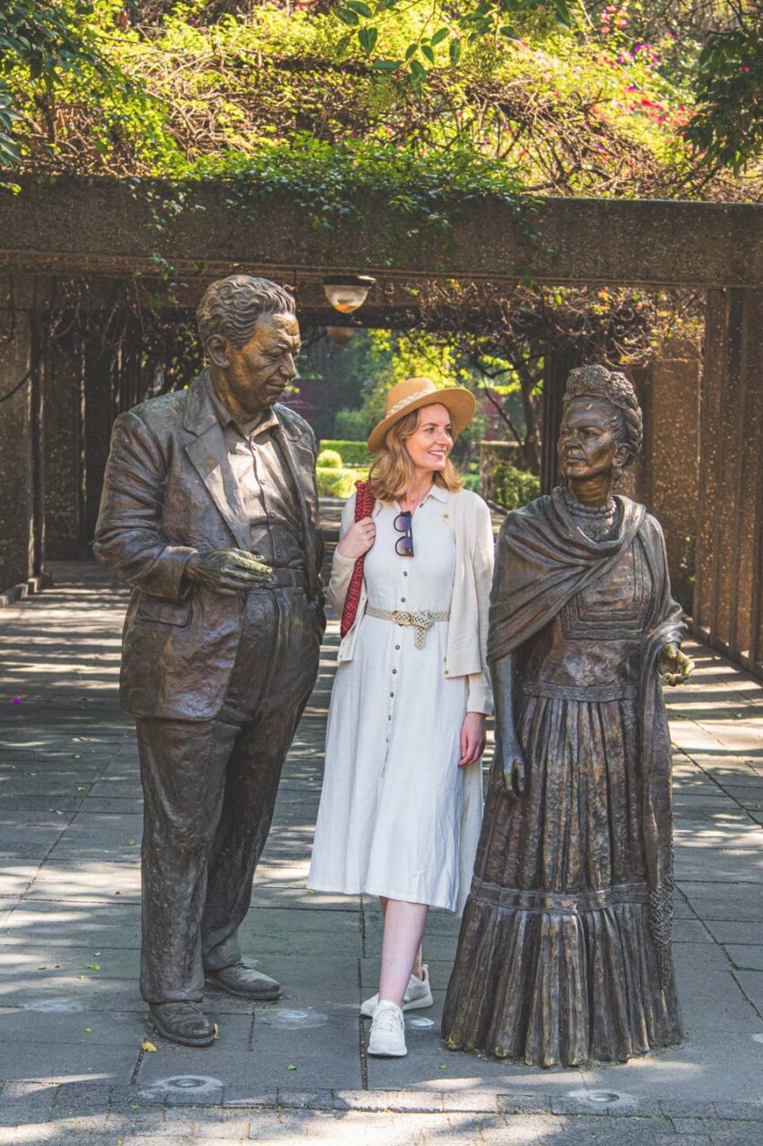 A woman walks among sculptures of Frida Kahlo and Diego Rivera in the Coyoacán district of Mexico City, in the green, peaceful surroundings of a park.