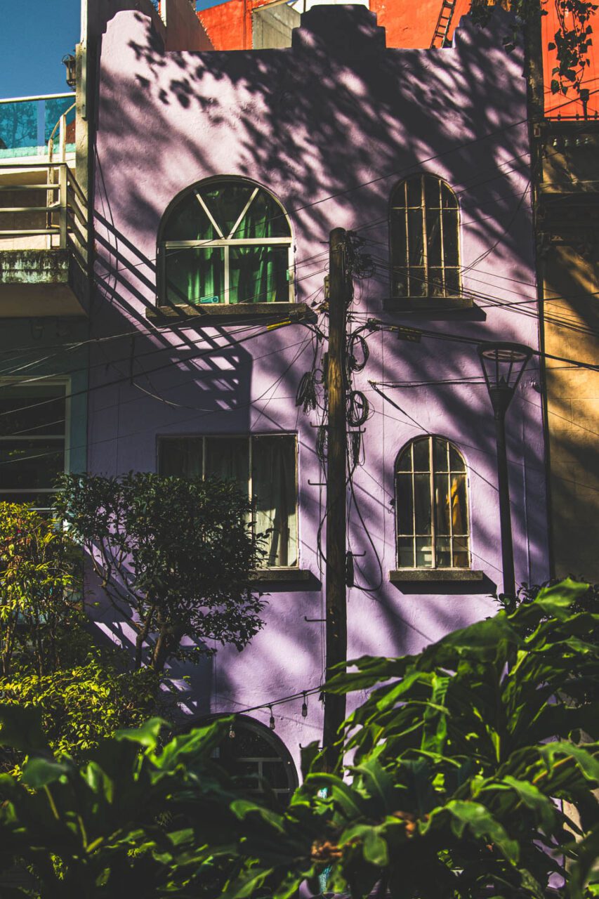 A colorful building in the Condesa district of Mexico City, with a purple facade, windows, and the shadow of trees; a peaceful afternoon in the city.
