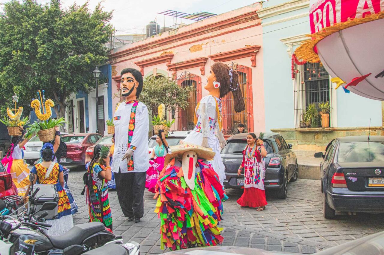 A street procession in Oaxaca featuring traditional costumes and puppets during a local festival.