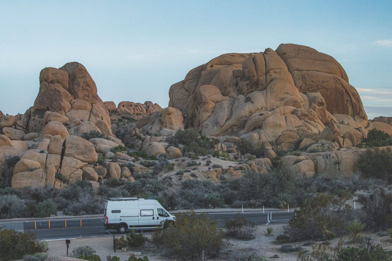 A white campervan against a backdrop of rocks in Joshua Tree.