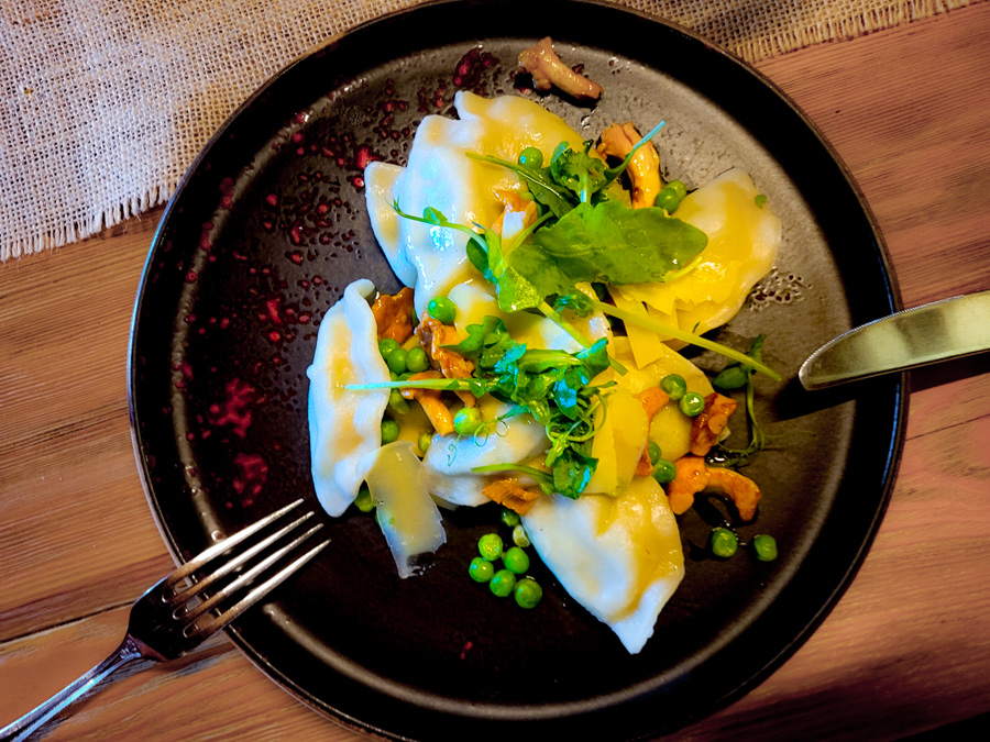 Talerz jesiennych pierogów z kurkami, zielonym groszkiem, rukolą i masłem na czarnym talerzu – rustykalna stylizacja.