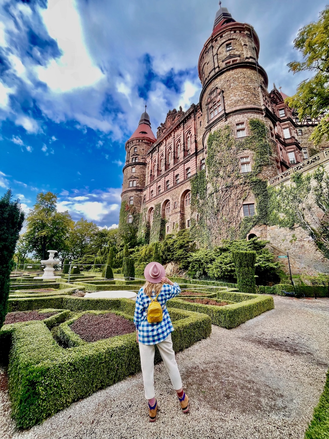 Kobieta w kapeluszu i plecaku zwiedza jesienią Zamek Książ w Polsce