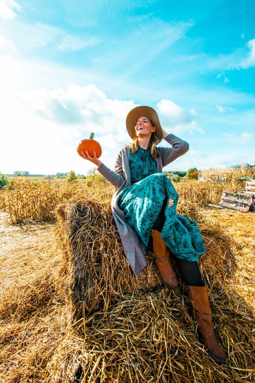 Kobieta siedząca na snopku siana z dynią na farmie dyniowej w słoneczny dzień