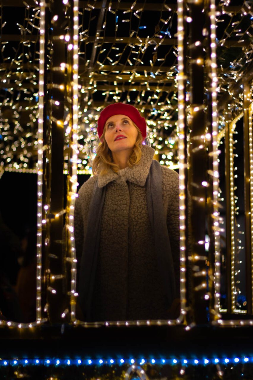 A woman in a red beret under festive lights at a Christmas market in Europe.