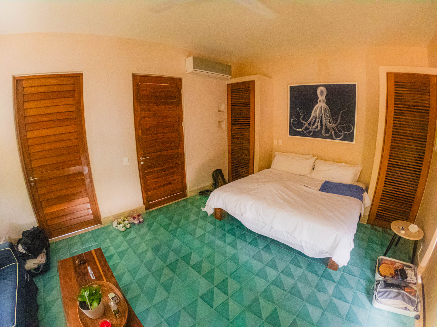 Jasny, przestronny pokój hotelowy z dużym łóżkiem, zieloną geometryczną podłogą, klimatyzacją i obrazem ośmiornicy nad łóżkiem w hotelu Tiki Tiki Tulum.