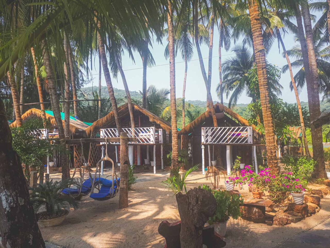 Colorful wooden beach huts among palm trees at Cozy Nook, Palolem, Goa