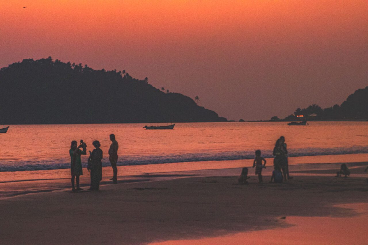 Sunset over Palolem Beach with silhouettes of people walking along the shore