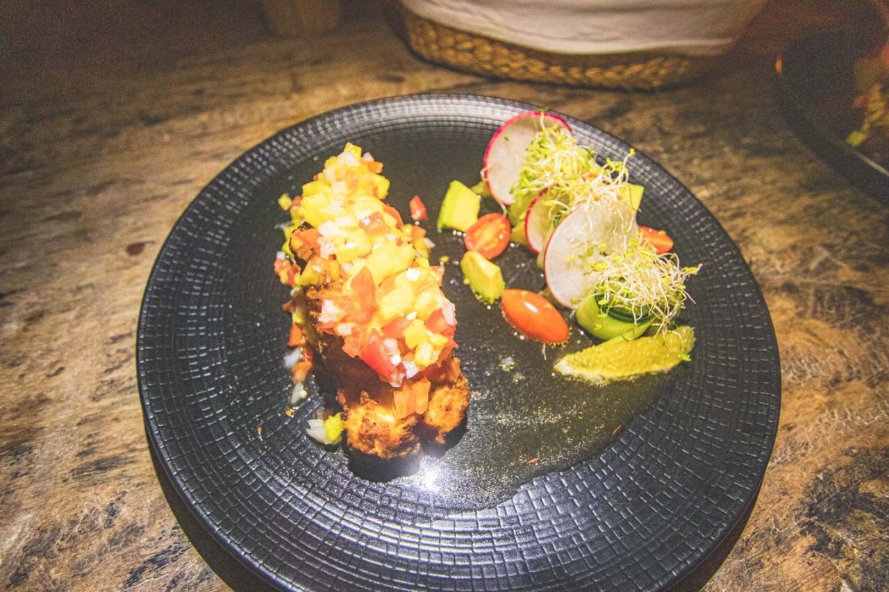 Kolorowe wegetariańskie danie na czarnym talerzu w rustykalnym stylu – mango salsa, awokado, pomidorki koktajlowe i kiełki, Isla Holbox.