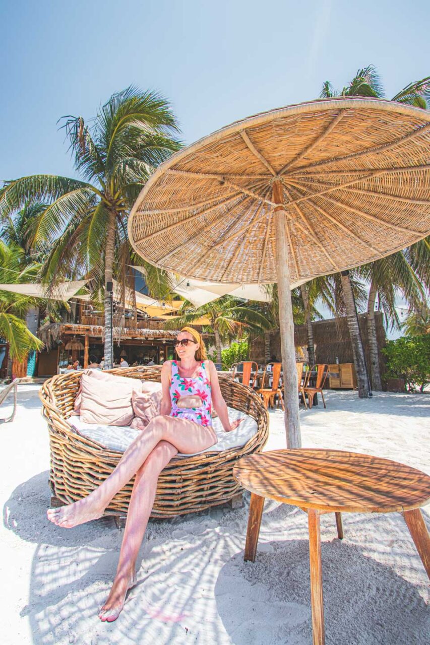 Kobieta odpoczywa w wiklinowym fotelu na plaży pod słomianym parasolem w Casa Las Tortugas – butikowym hotelu na Isla Holbox.