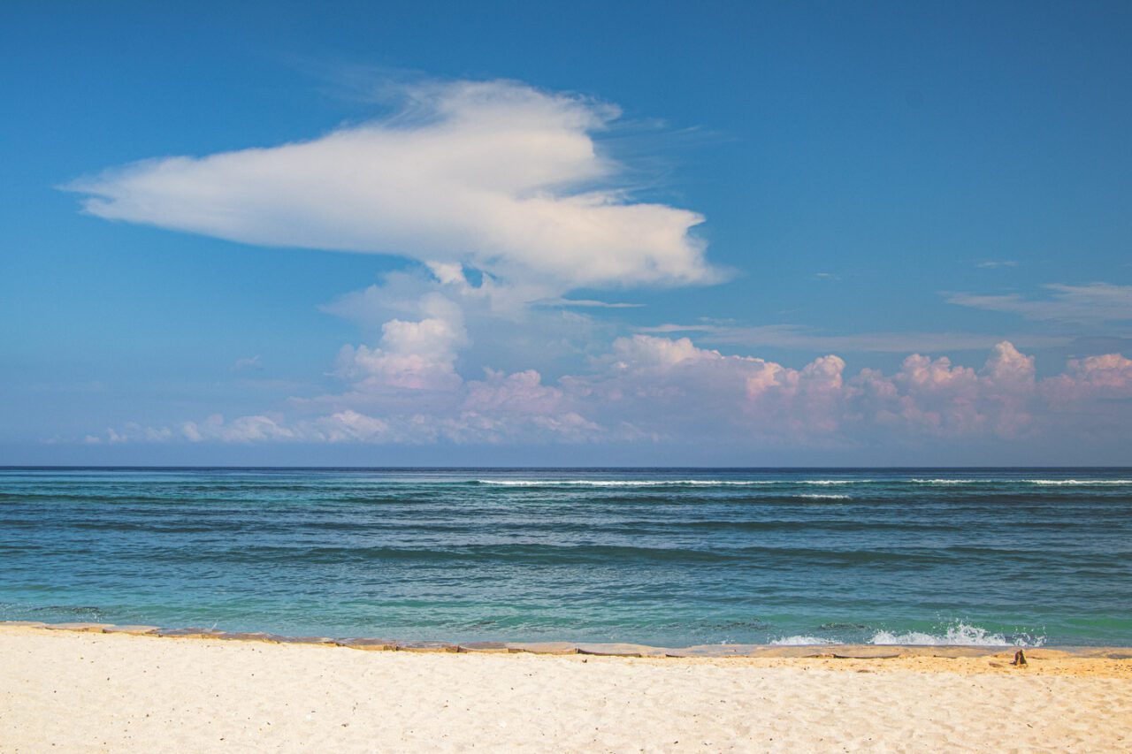 Morning view of Gili Trawangan’s west beach with white sand, turquoise water and soft, painted-looking clouds.