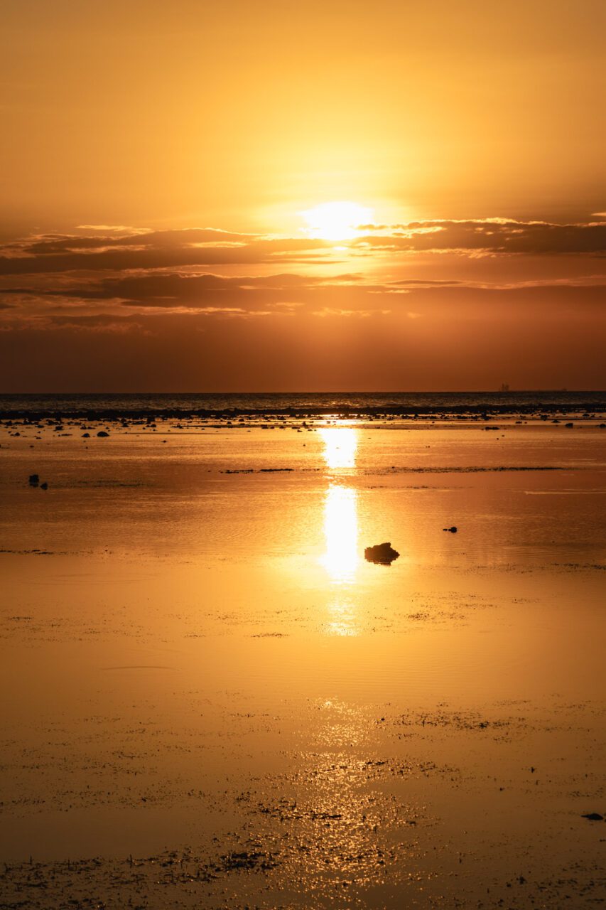Golden hour on Gili Trawangan with calm sea reflecting the sky and the sun setting over the horizon.