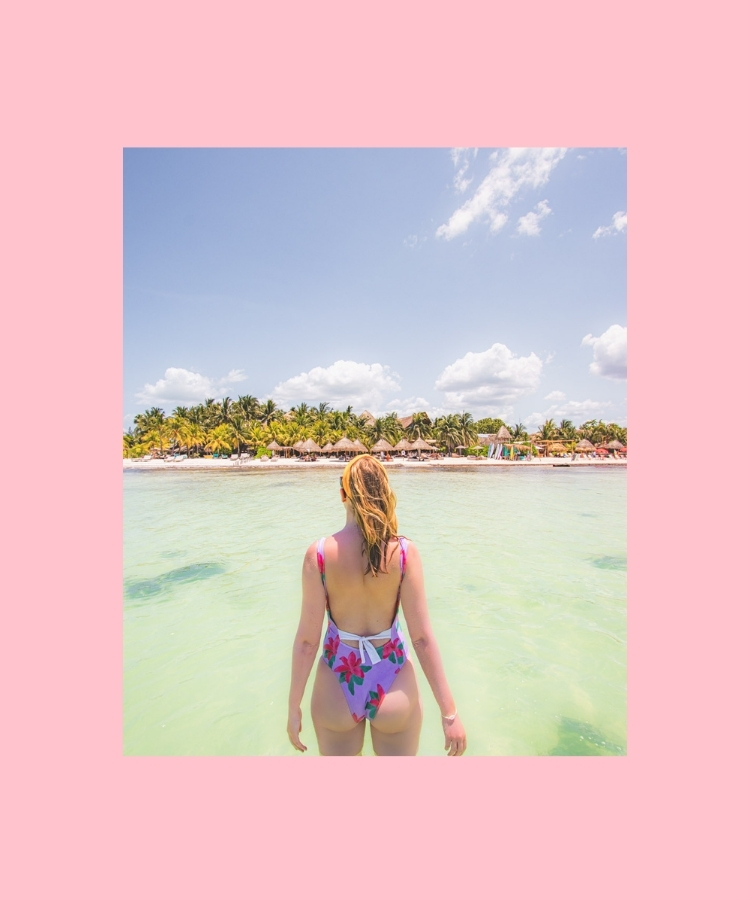 A woman standing in turquoise water on a beach in Mexico, with palm trees in the background.