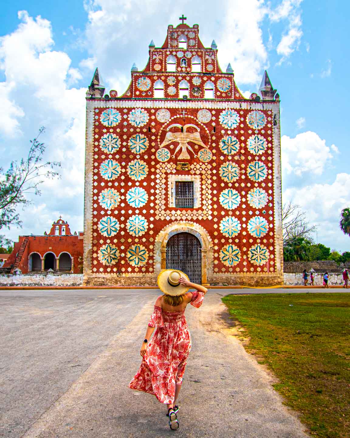 A woman wearing a hat walking toward the colorful façade of the church in Uayma, Mexico.