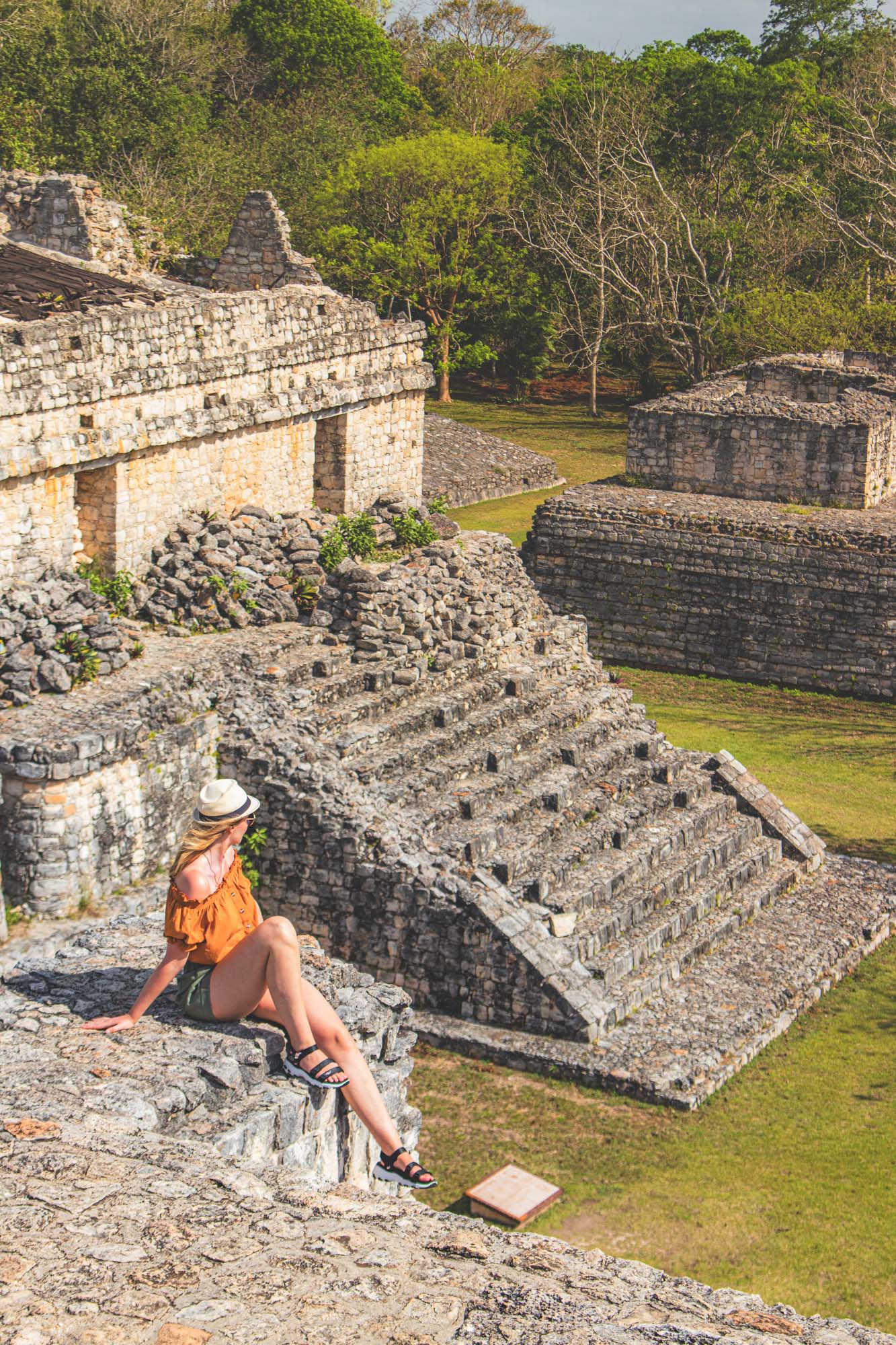 A woman sitting on a stone wall and looking at the ancient Mayan pyramids in Ek Balam