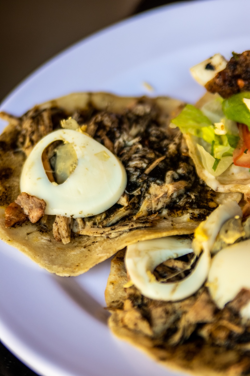 Close-up of traditional Mexican tacos with meat, sauce, and slices of boiled egg.