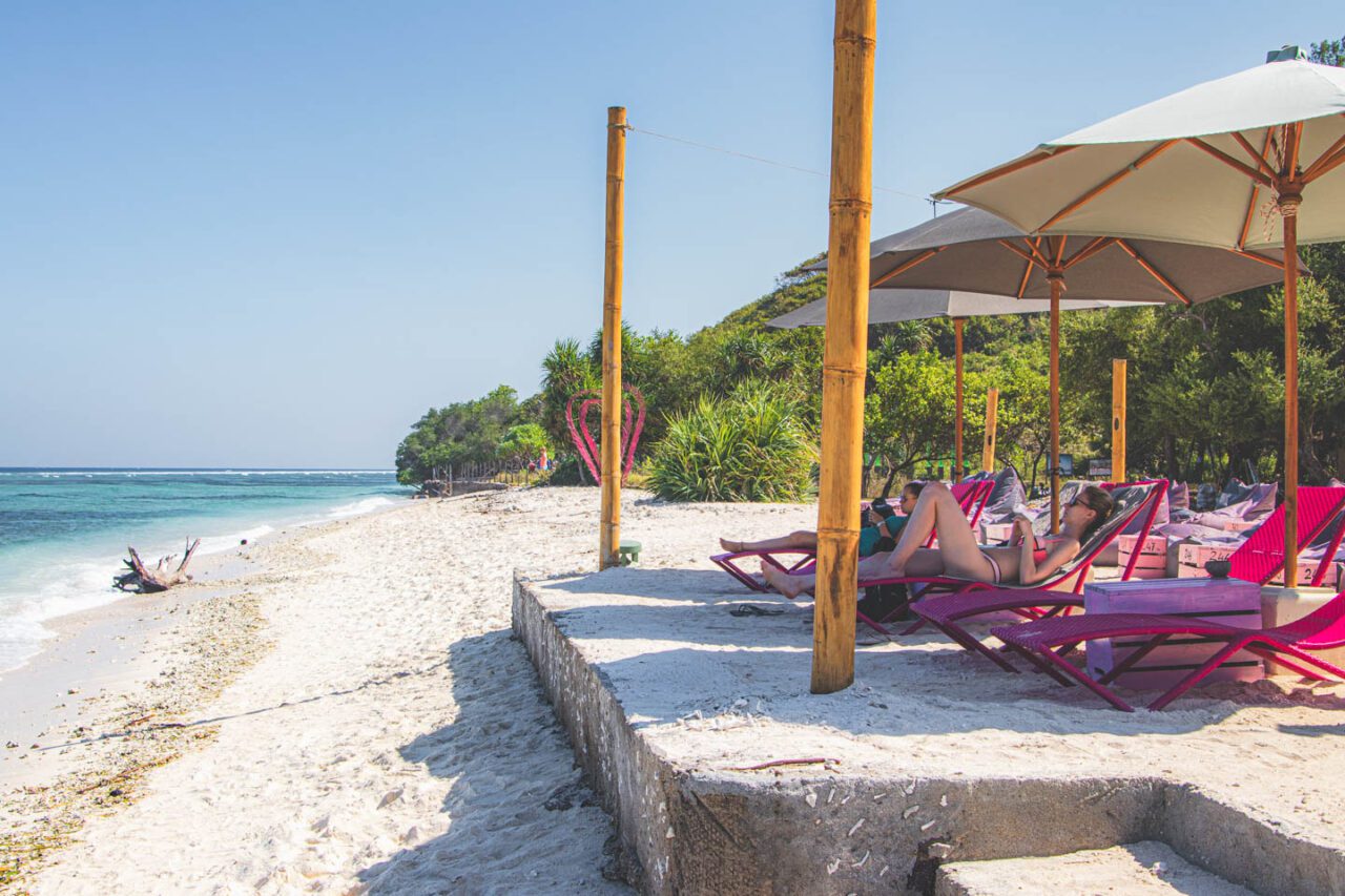 Plaża na Gili Trawangan z różowymi leżakami, bambusowymi parasolami i turkusowym morzem w tle.