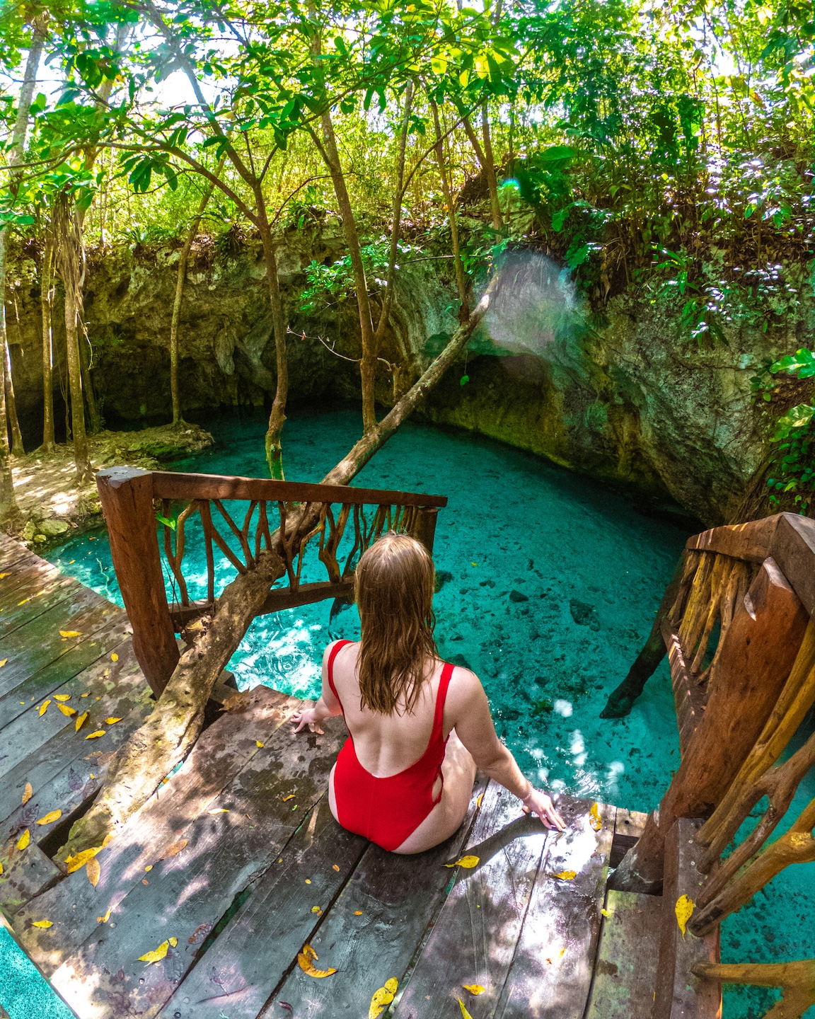 A woman in a red swimsuit sits at a cenote in the jungle near Tulum, Mexico.