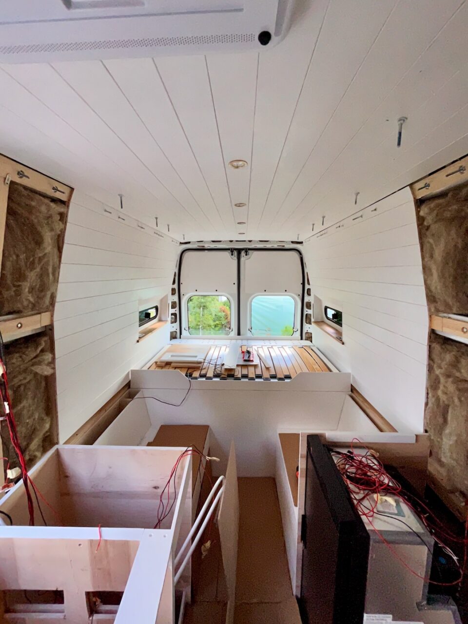 Camper interior under construction – white paneling, fold-out bed, and electrical installation.